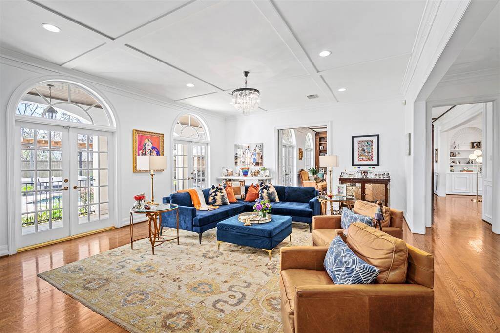 Spacious family room has a custom carved limestone fireplace, beautiful molding, cross-beamed ceilings and double palladium French doors that look out to the beautiful pool and landscaping