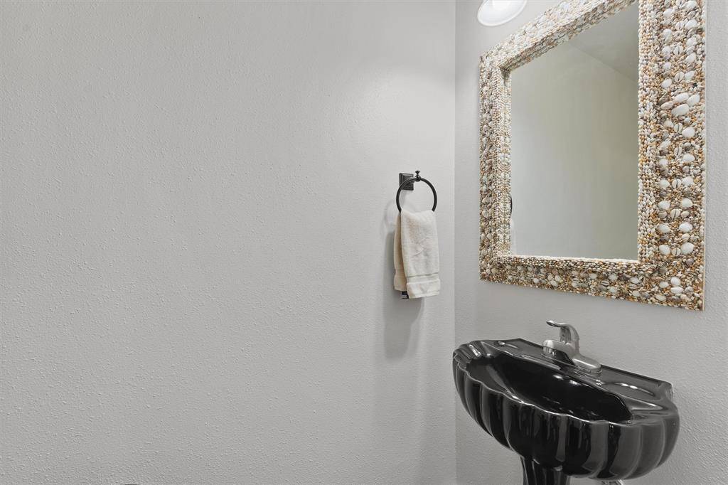 A stylish powder room on the first floor with a shell-adorned mirror and unique black seashell sink adds a touch of coastal flair.