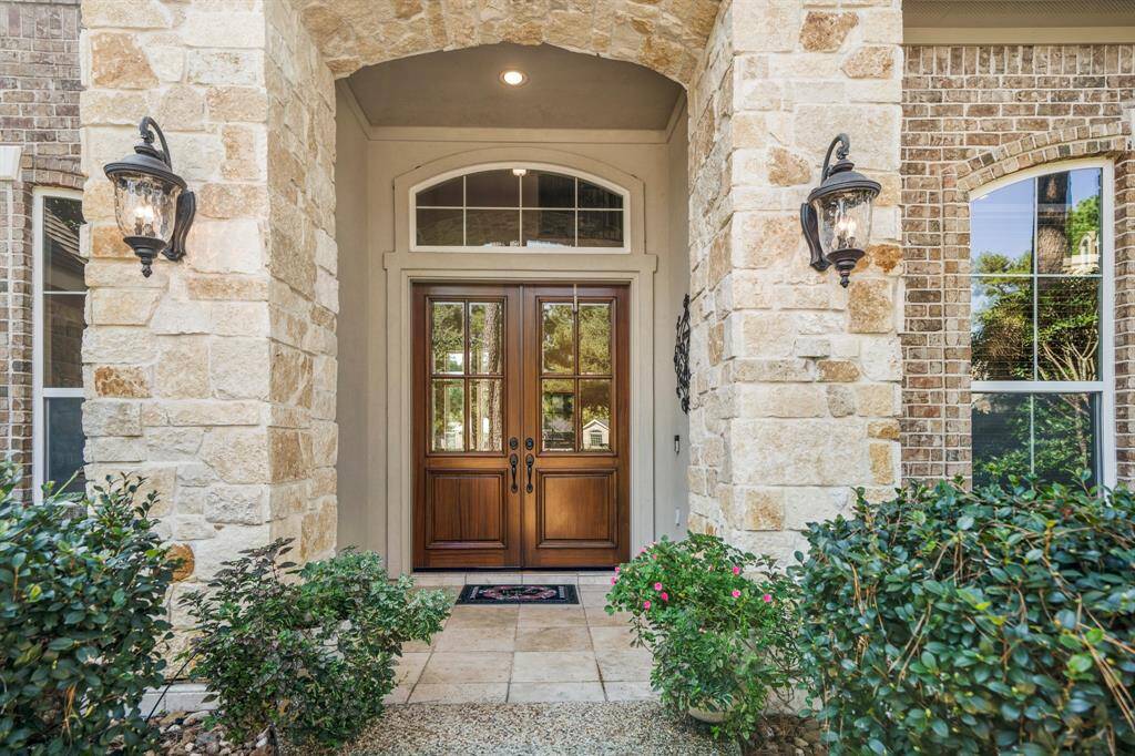 Beautiful stacked stone elevation welcoming covered front porch with coach lighting flanking the arched entryway leading to double wood doors.