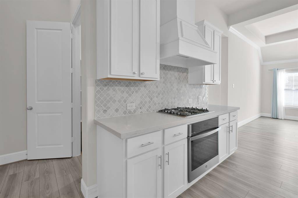 Stylish and modern kitchen featuring Quartz countertops, white cabinetry with hardware, a gas cooktop, stainless appliances REFRIGERATOR INCLUDED, contemporary backsplash and walk in pantry