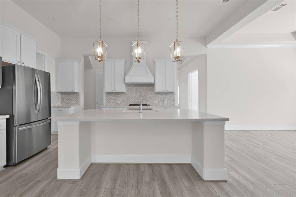 The chef's kitchen boasts modern lighting, an oversized island with Quartz countertops, high end finishes and stainless steel appliances