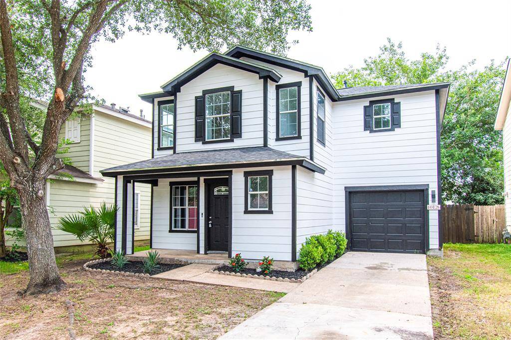 Charming two-story home with modern black and white exterior. Features include a covered front porch, attached garage, and a well-kept yard with mature trees. Ideal for those seeking a stylish and inviting residence.