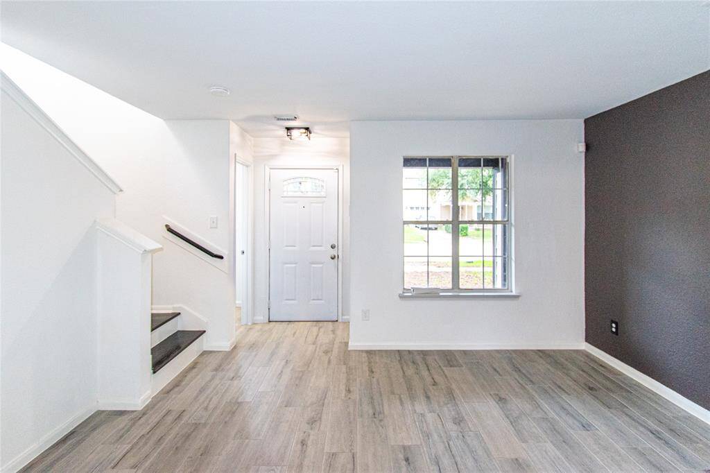 Inviting entryway with light wood flooring, a large window, and a neutral color palette. Stairs lead up with dark accents providing contrast. Ideal for welcoming guests.