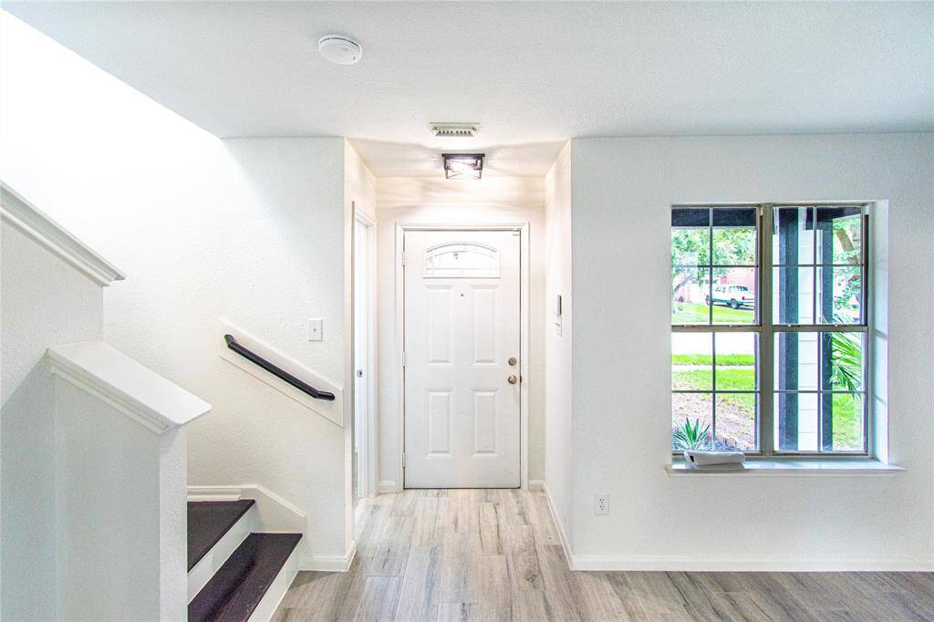 Bright entryway with a modern front door, adjacent staircase, and large window offering natural light. Wood-look flooring enhances the welcoming atmosphere.