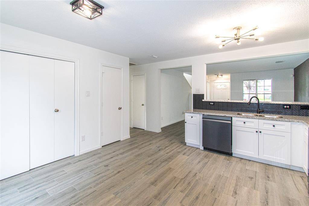 Kitchen and adjacent area with sleek wood-style flooring, white cabinetry, and stainless steel appliances. The open layout offers a view into a well-lit living space, enhancing the home's airy feel.