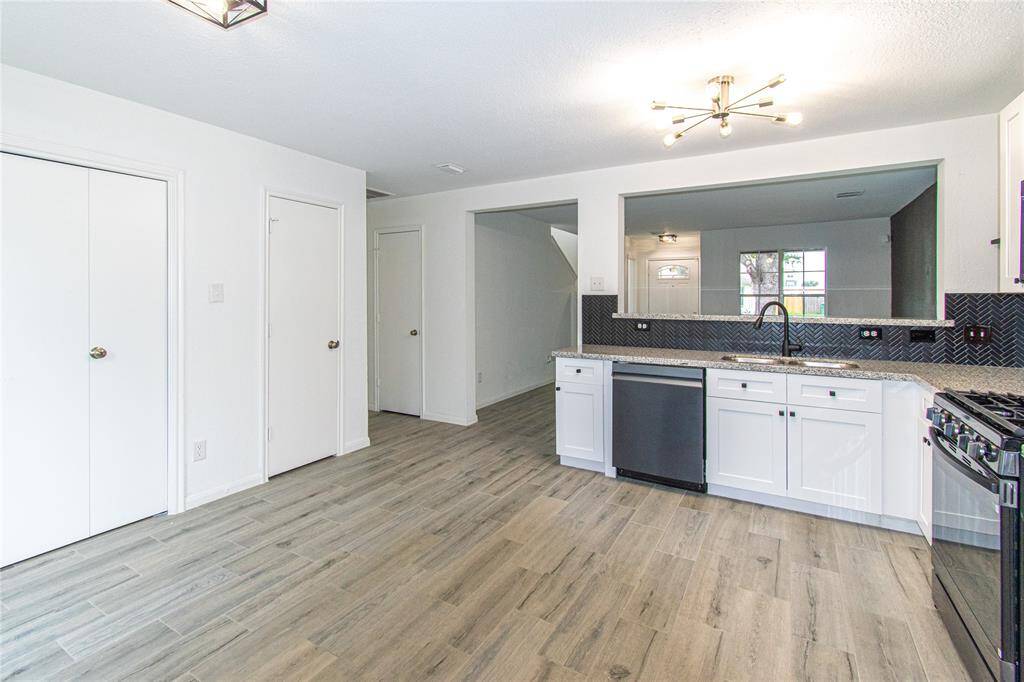 Kitchen with white cabinetry, granite countertops, and stainless steel appliances. The open layout leads into a spacious living area, featuring light wood flooring and ample natural light.