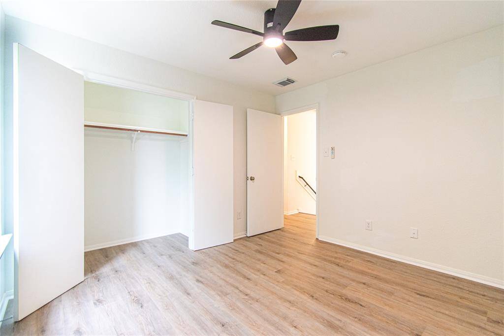 This room features fresh white walls, wood-look flooring, and a ceiling fan. It includes a closet with double doors and has good natural light from a large window.