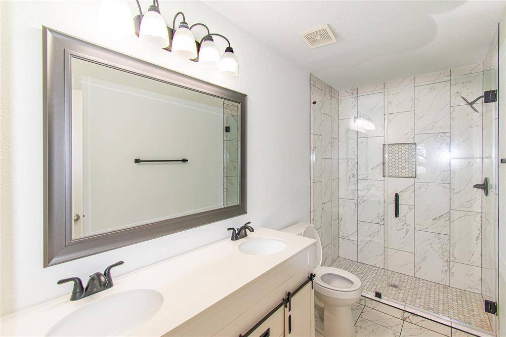 Modern bathroom featuring a spacious glass-enclosed shower with elegant tile work. It includes a double vanity with sleek fixtures and a large framed mirror, creating a bright and inviting space.