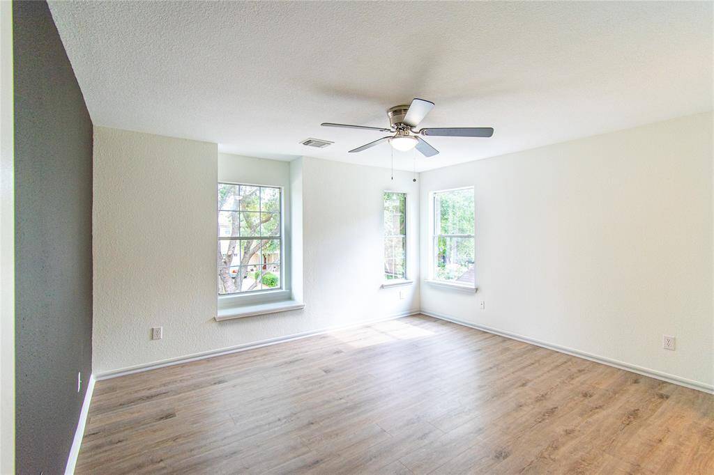Bright room with large windows, wood flooring, and a ceiling fan. Ideal for a cozy living space or bedroom.