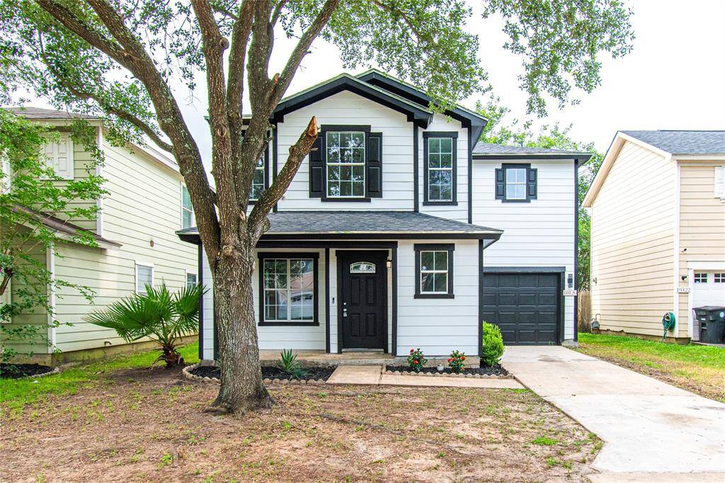 This is a charming two-story home with a modern black and white exterior. It features a welcoming front porch, large windows, and an attached single-car garage. The property has a simple front yard with mature trees, offering shade and curb appeal.