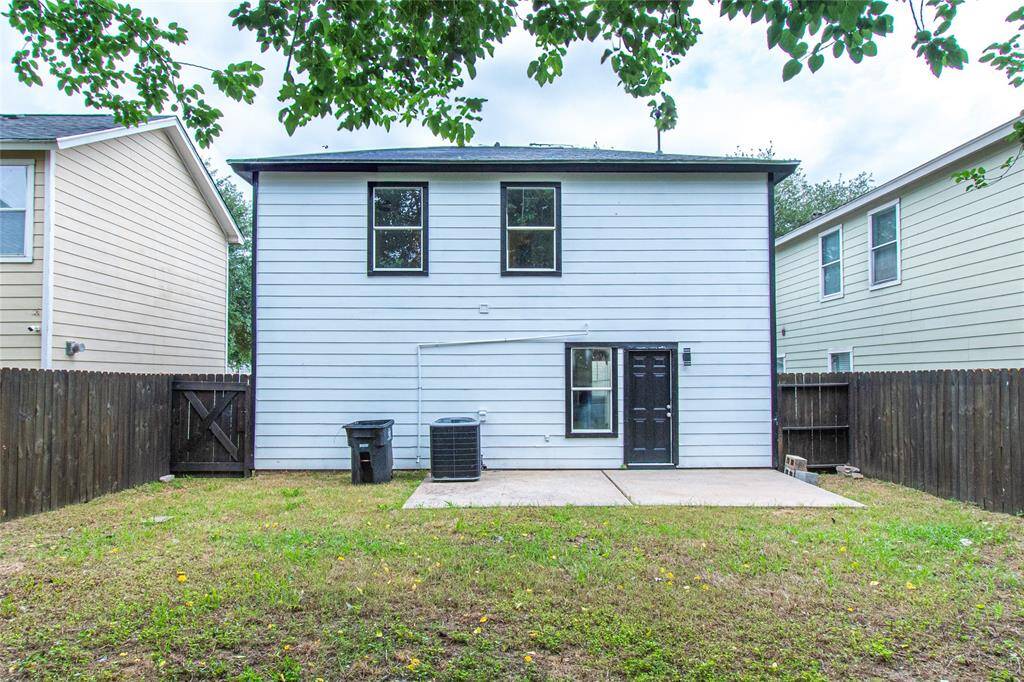 The back of a two-story home with white siding, featuring a small fenced backyard with a concrete patio. There are two upper windows and a back door, offering a simple and functional outdoor space.