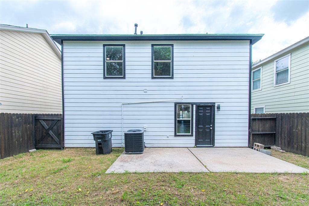 House with white siding and black trim. It features two large windows, a small concrete patio, and a fenced backyard. The space includes an outdoor air conditioning unit.