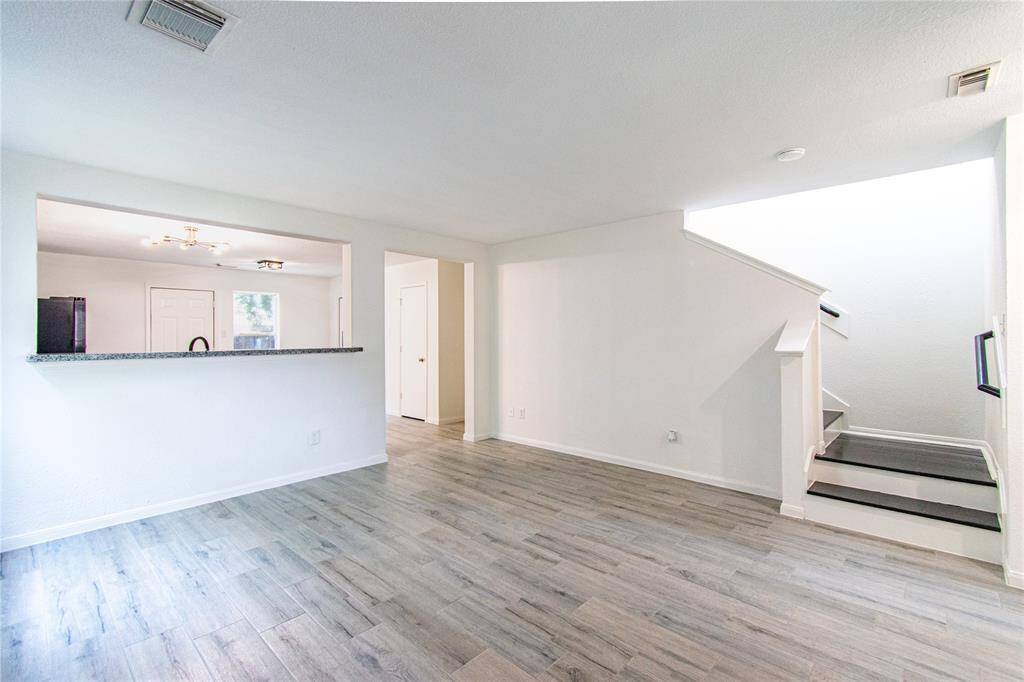 Open-concept living space with light wood flooring, a modern staircase, and a kitchen pass-through. The white walls enhance the natural light, creating an inviting atmosphere.