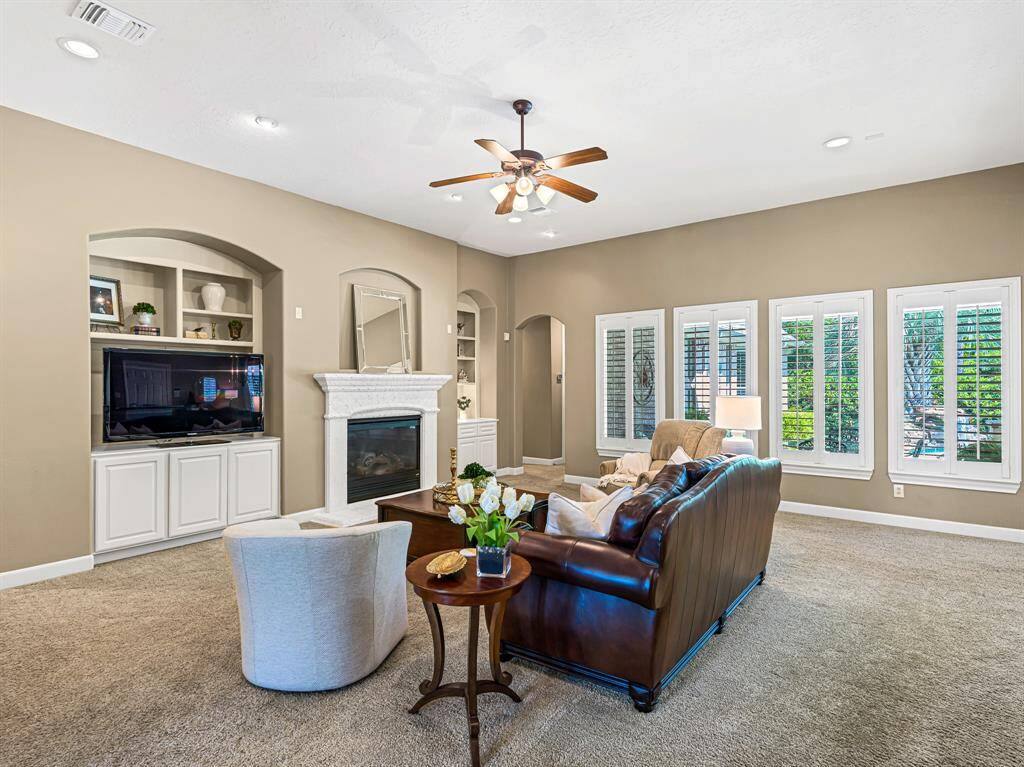 The spacious family room offers a cozy, inviting atmosphere, featuring a well-designed media niche with built-in cabinets & shelving that provide ample storage & display space. A wall of windows overlooks the backyard oasis, beautifully framed with plantation shutters to allow natural light in while maintaining privacy.
