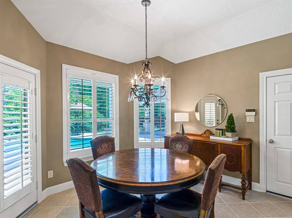 The bright breakfast area seamlessly connects the family room and kitchen, featuring an elegant 5-arm chandelier that adds a touch of sophistication. A large bay window with plantation shutters fills the space with natural light, while 14-inch tile flooring and 5-inch baseboards add both style and durability.