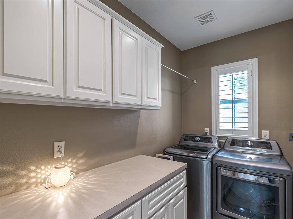 The laundry room is both functional and bright, featuring crisp white cabinetry that offers ample storage, along with a spacious 5-foot countertop—perfect for folding laundry. A built-in hanging rod provides a convenient space for air-drying delicates, while a large window fills the room with natural light.