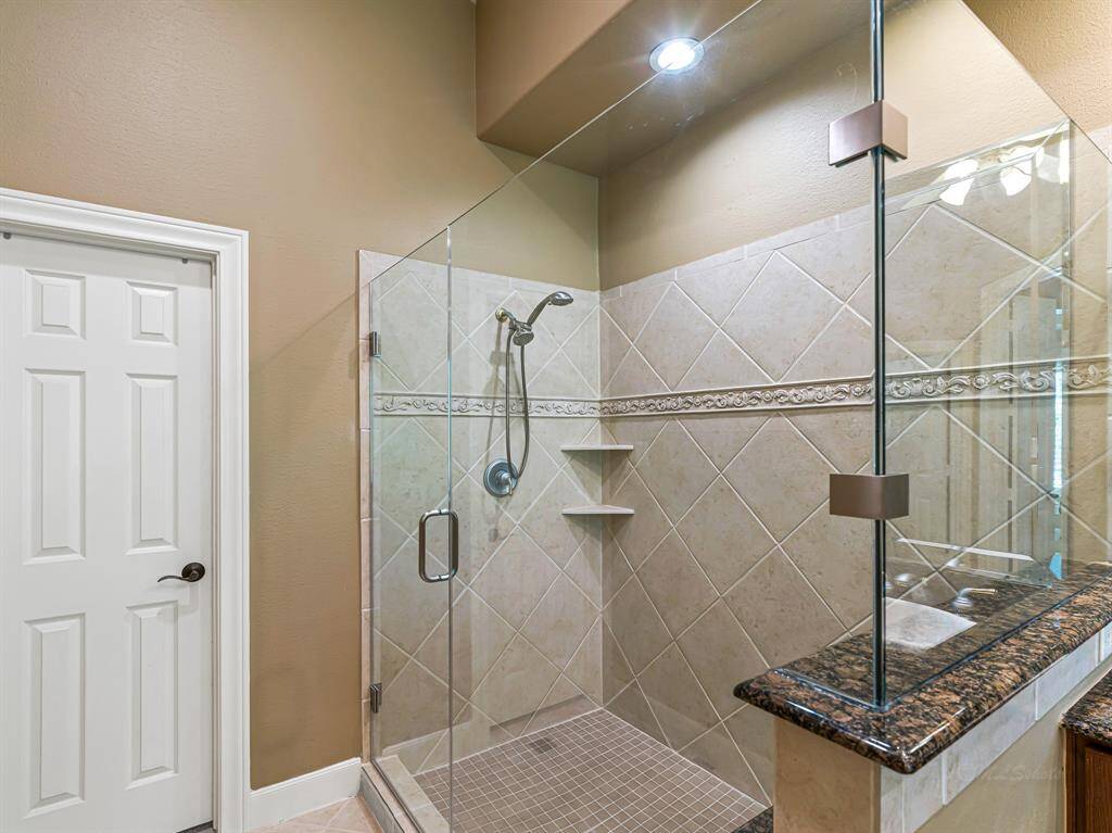The frameless glass shower showcases a pristine tile surround accented with delicate tumbled stone detailing and includes a granite bench for added comfort. A dual shower head system provides a spa-like experience.