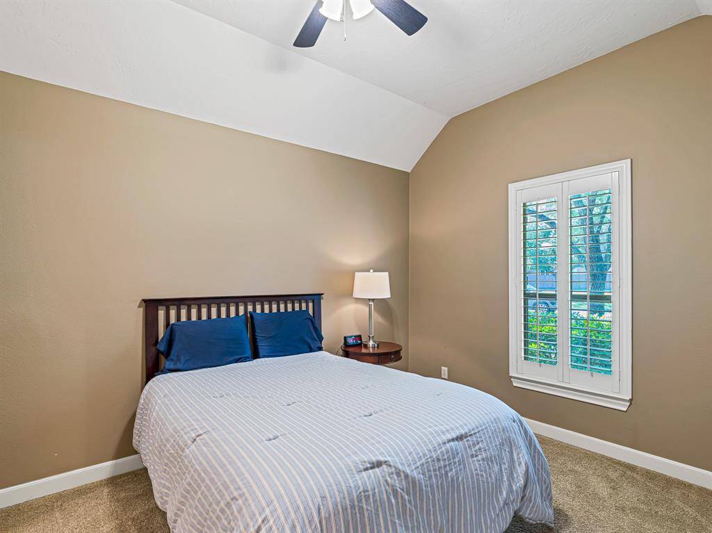 This spacious secondary bedroom features a large walk-in closet, plantation shutters, plush carpet, 5-inch baseboards, and a high ceiling with a fan—offering comfort and style.