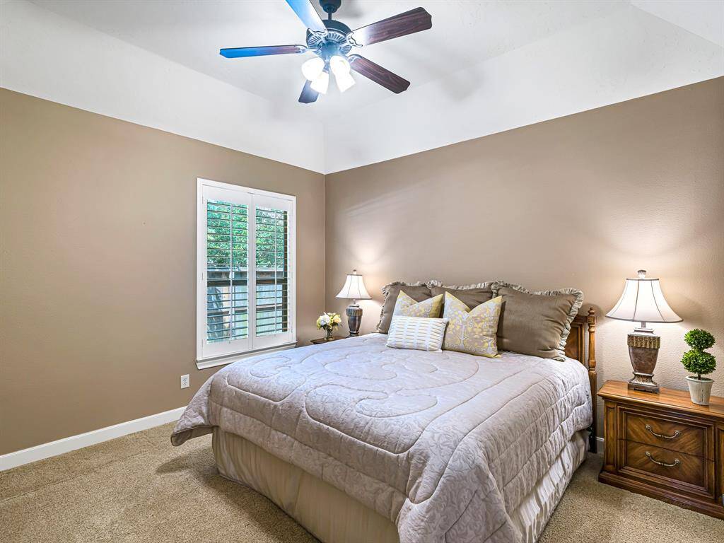 This spacious secondary bedroom features plantation shutters, plush carpet, 5-inch baseboards, a high ceiling with a fan and a large walk-in closet.