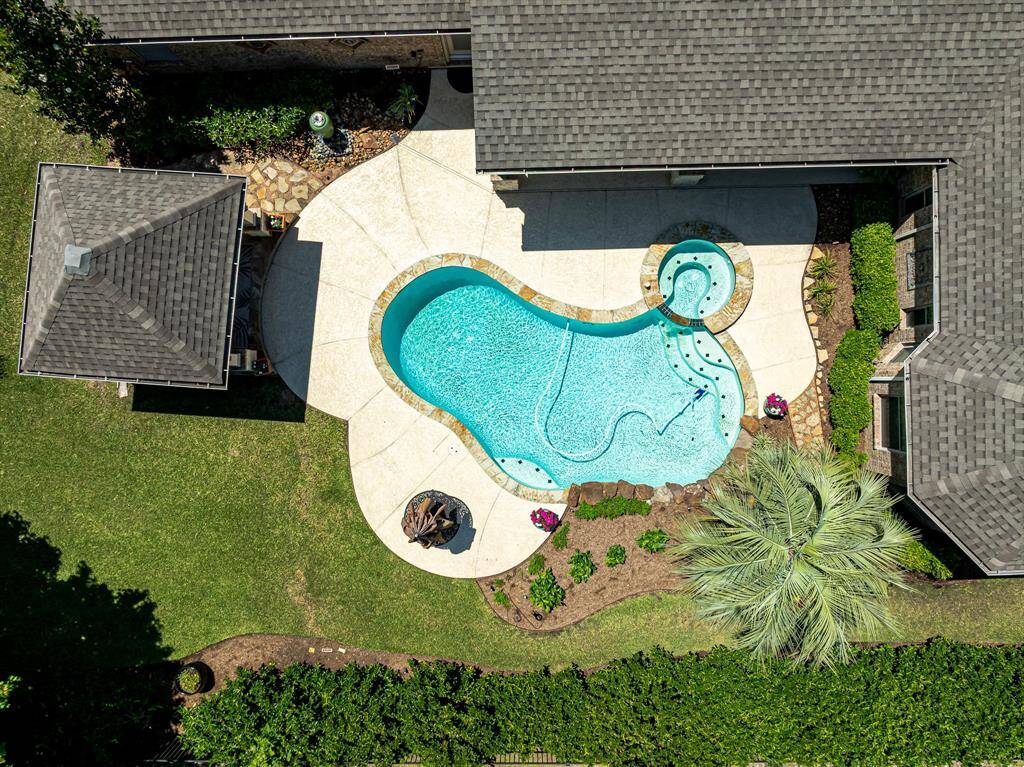 This aerial view showcases the expansive backyard oasis, featuring a sparkling pool and spa, a charming cabana, lush green lawn, and a cool deck patio—perfect for relaxing or entertaining in style.