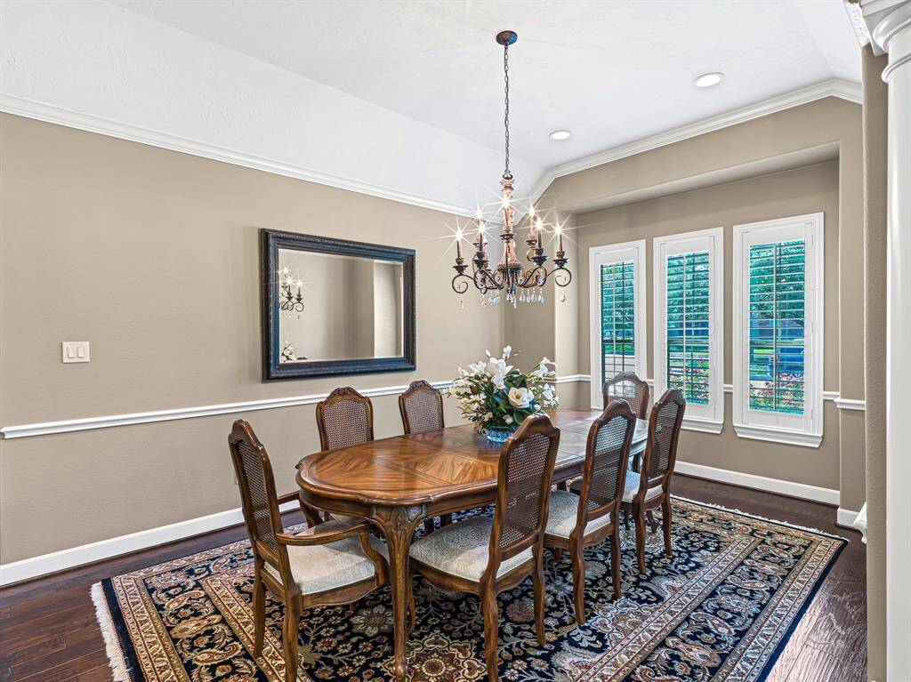 The formal dining room is a masterpiece of elegance, with a stunning 9-arm wrought iron chandelier, adorned with crystal details, serving as the dramatic focal point. Bay windows flood the space with natural light, creating a bright atmosphere. Recessed lighting enhances the room's charm, offering a warm & inviting glow.