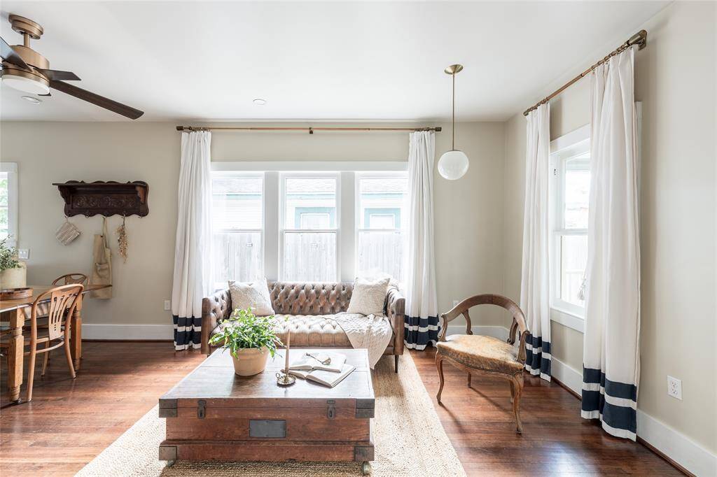 Layered in natural light, the living room invites comfort with curated textures, a vintage tufted sofa, and timeless charm framed by tall windows.