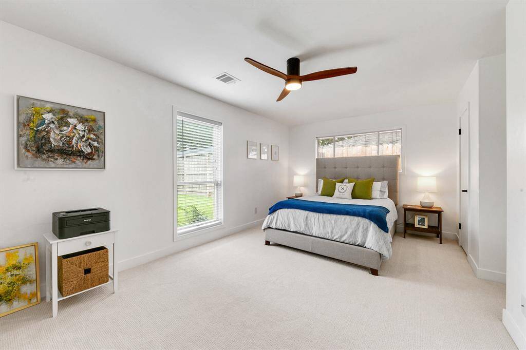 A bright and spacious bedroom featuring a large window, modern ceiling fan, and plush carpeting.