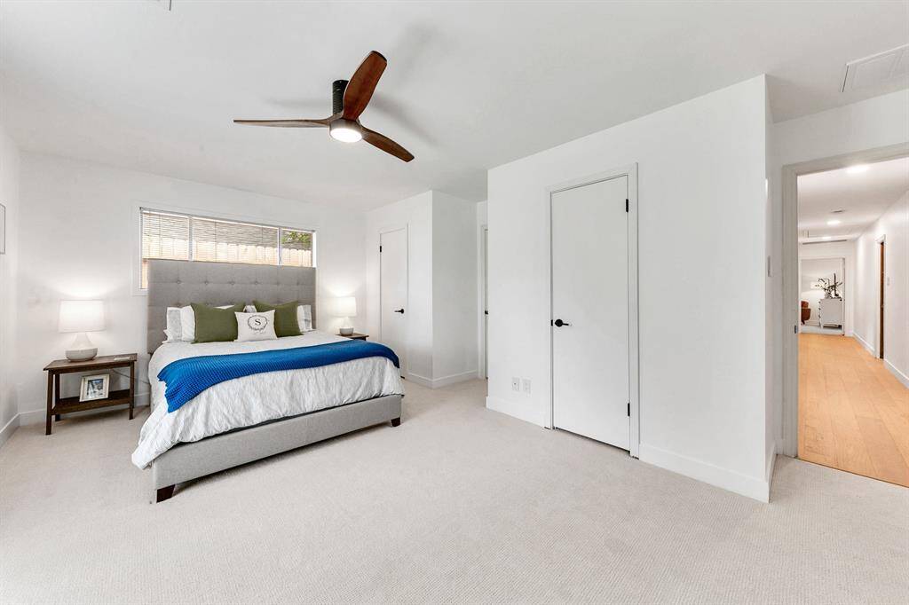Spacious, bright bedroom with a contemporary design. Ample natural light through a wide window, and a hallway leads to additional living areas.