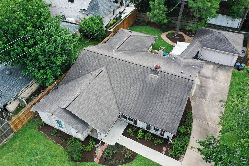 This aerial view showcases a charming single-story home with a well-maintained lawn and mature trees. The property features a spacious driveway leading to a detached garage, and a fenced backyard offering privacy