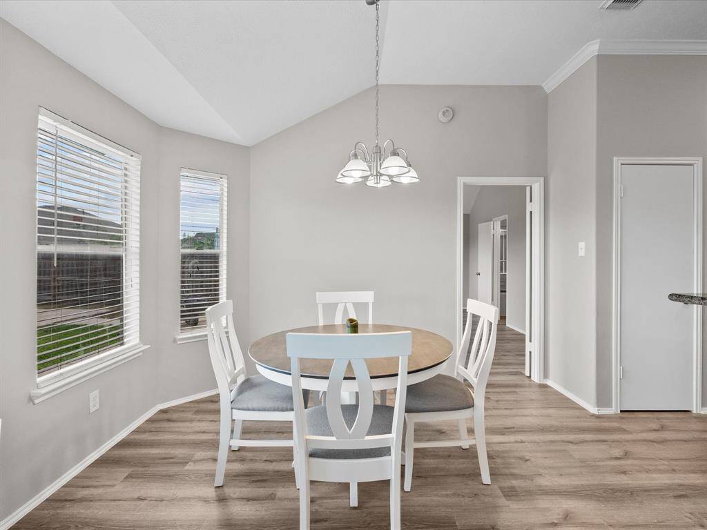 Another bright dining area with wood look flooring, neutral walls, and large windows providing ample natural light.
