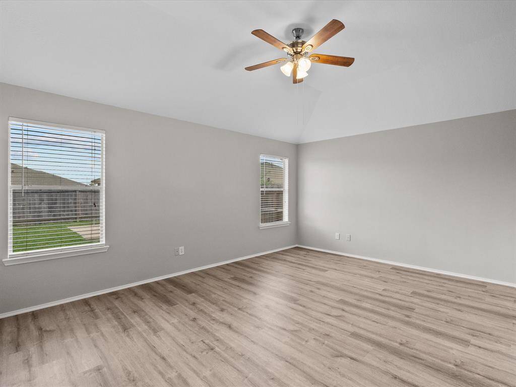 This spacious bedroom has more LVT flooring, neutral walls, and a ceiling fan. Two large windows provide ample natural light and offer a view of the backyard.