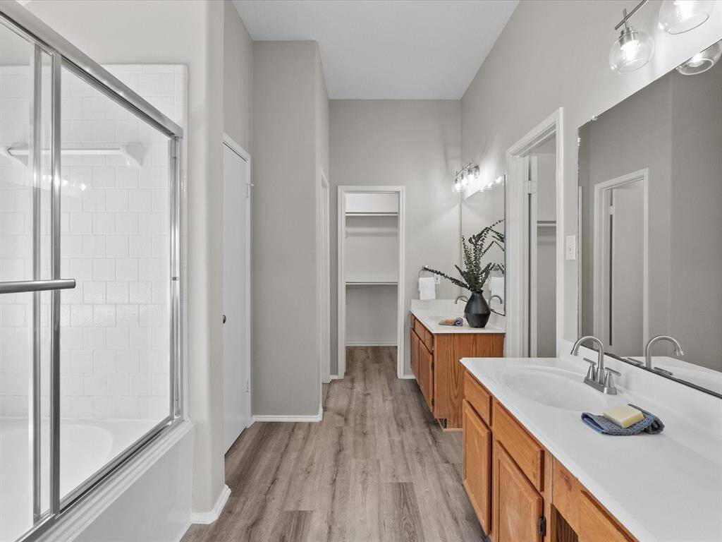 It includes a glass-enclosed shower with a bathtub and a walk-in closet, all set on stylish LVT flooring that extends into the bathroom and closet.