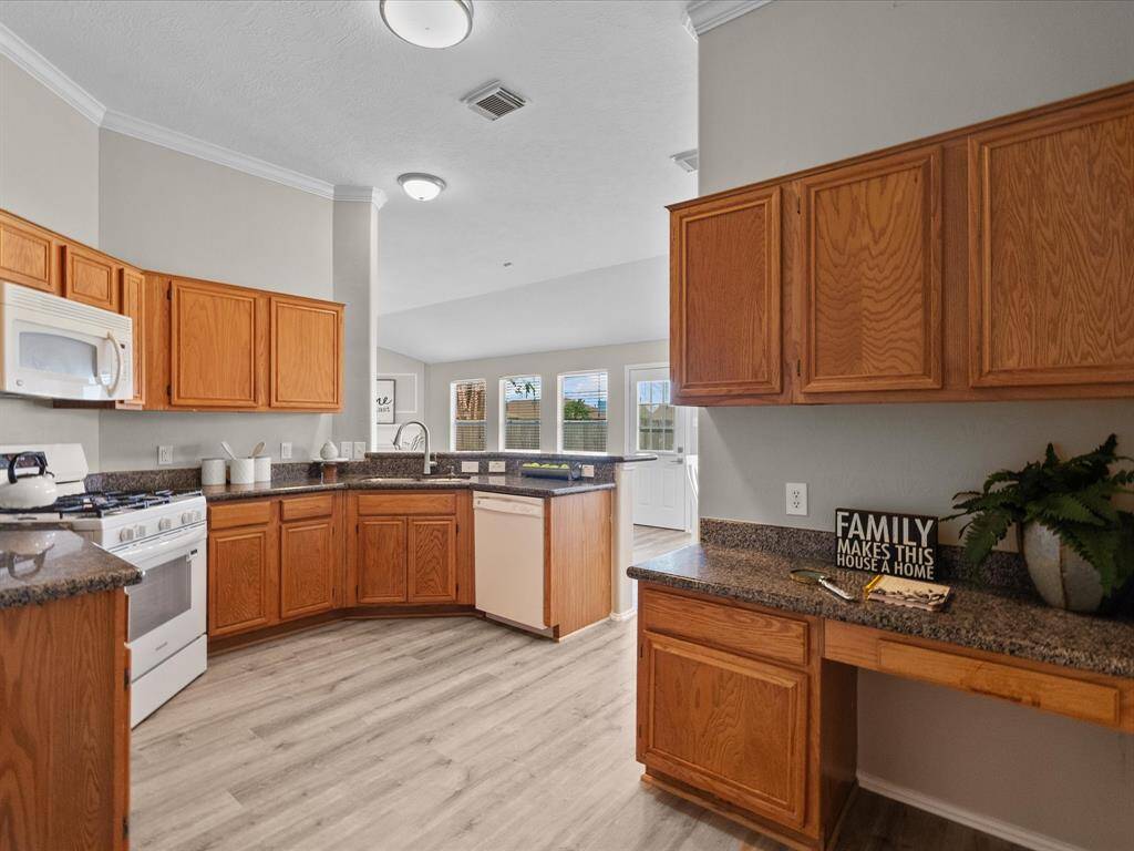 Bright and spacious kitchen featuring warm wood cabinetry, granite countertops, and modern appliances. The open layout flows into the living area, creating a welcoming space for family gatherings. Natural light enhances the inviting atmosphere.