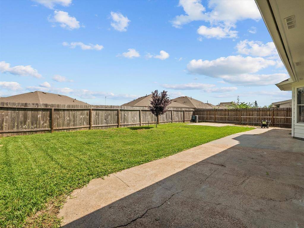 Spacious backyard with a well-maintained lawn, a small tree, and a privacy fence. There's a large concrete patio perfect for outdoor activities and relaxation.