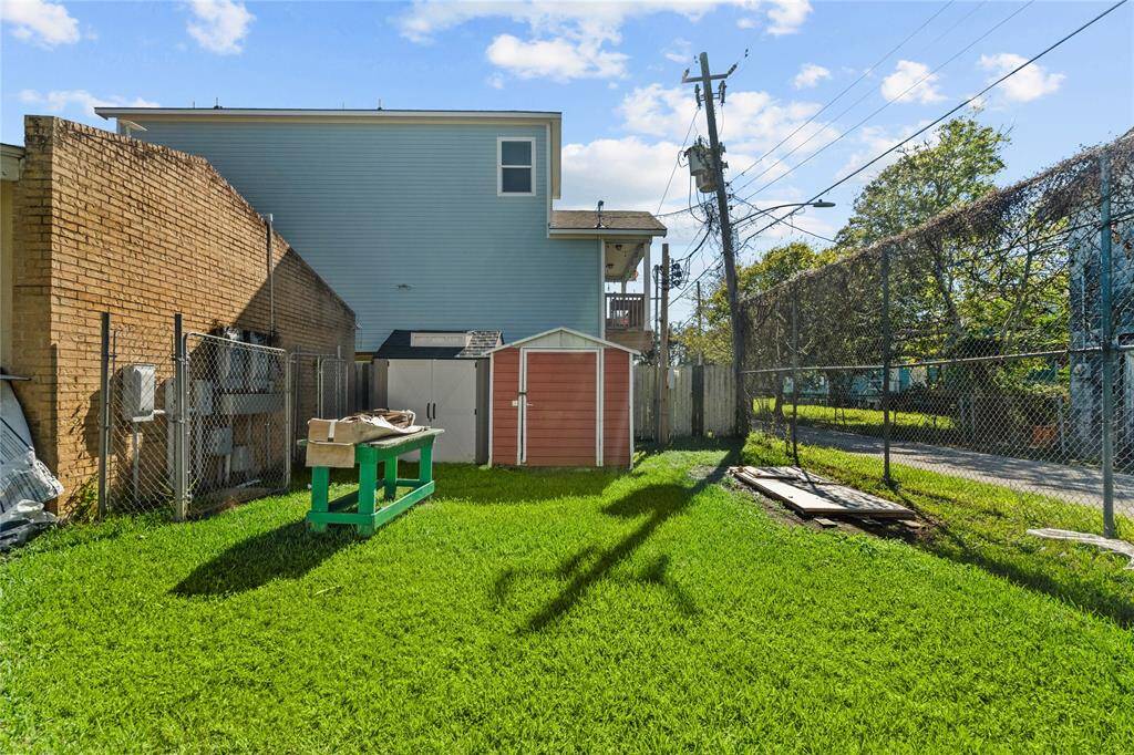 This spacious outdoor area has lush grass, some outdoor sheds, and a tall chain-link fence that borders the property.