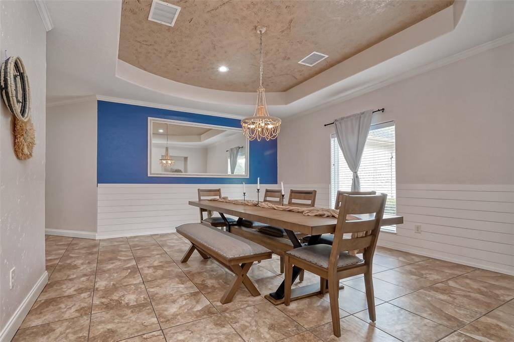 Dining Room Full View – Stylish formal dining room with a tray ceiling, chandelier, accent wall with oversized mirror, and seating for eight, including a comfortable bench.
