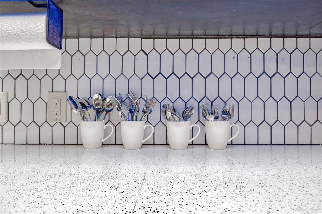 Kitchen Utensil Display – Creative organization meets functionality with silverware beautifully stored in matching white mugs, backed by modern vertical tile and under-cabinet lighting.