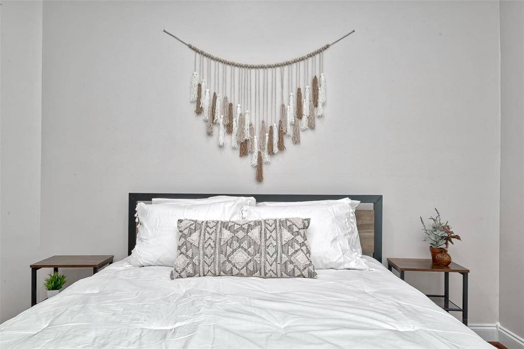 Crisp white linens and a cozy, textured headboard wall create a serene atmosphere in this charming and inviting bedroom.