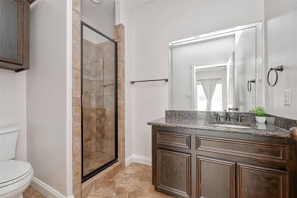 The guest bathroom features a walk-in tile shower, granite countertops, and warm-toned finishes that blend functionality and style.