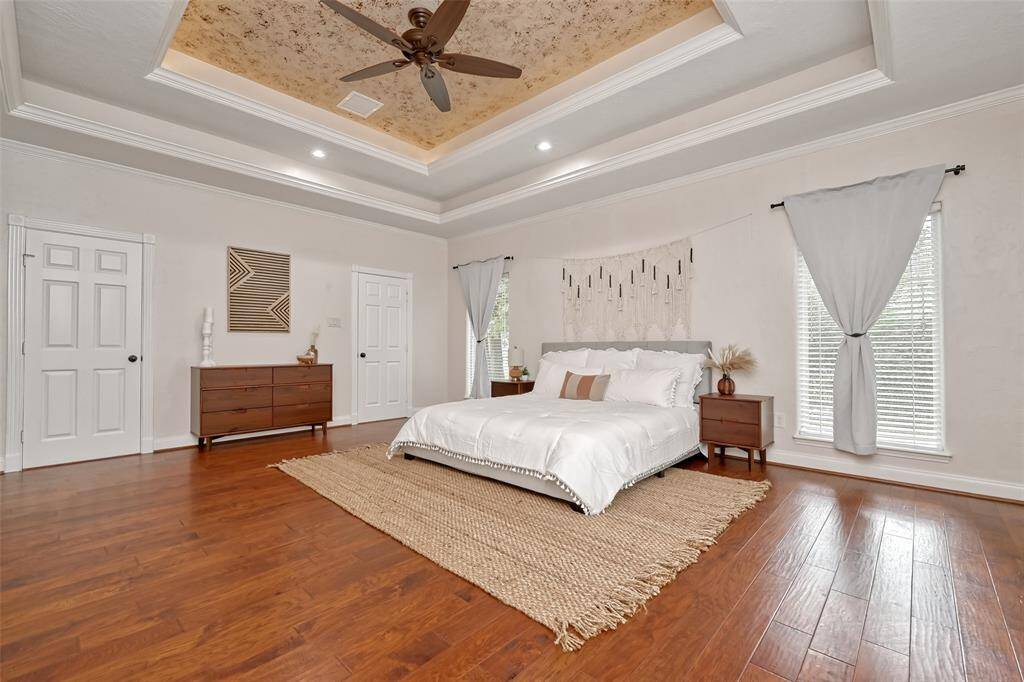 The expansive primary bedroom is an oasis of calm, highlighted by a tray ceiling, hardwood floors, and sophisticated neutral tones.