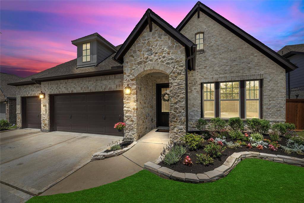 This charming David Weekley home features a stone and brick exterior with a welcoming archway, a spacious three-car garage, and a beautifully landscaped front yard.