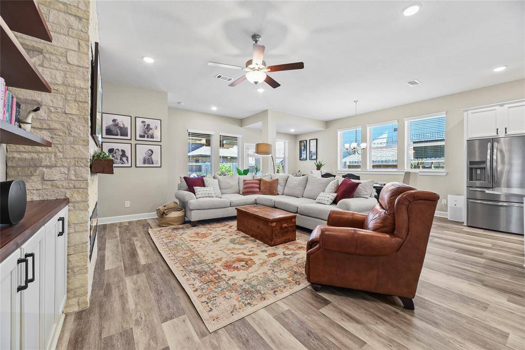 This spacious living room features an open layout with a stone stacked fireplace, LPV flooring, and ample natural light from large windows.  The adjacent dining area and kitchen create a seamless flow, perfect for entertaining.
