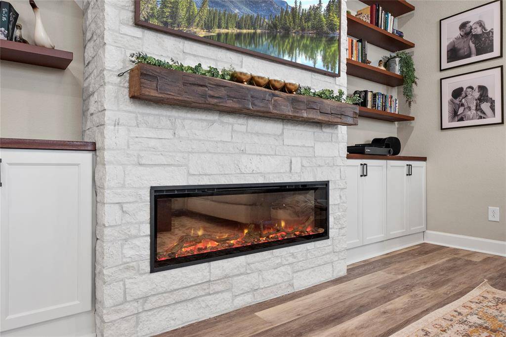 This living space features a white stone fireplace with a modern electric insert, complemented by a rustic wooden mantle. Built-in shelves and cabinets provide ample storage, while decorative touches.