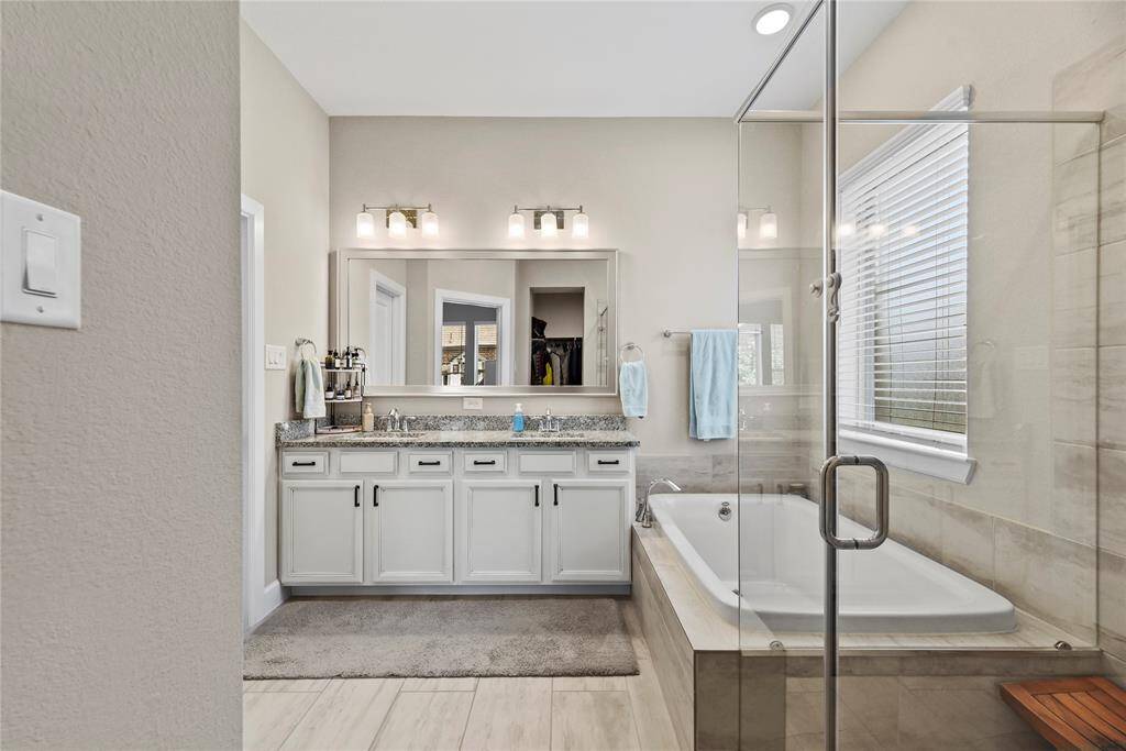 The primary bathroom features a double vanity with granite countertops, large mirror, a spacious glass-enclosed shower and a separate soaking bathtub.