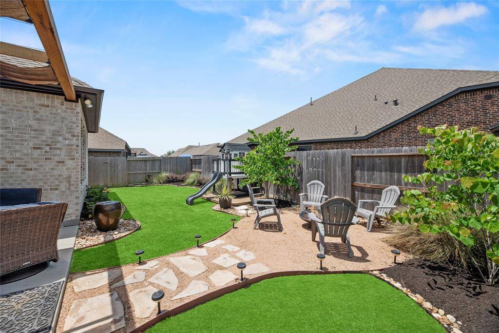This backyard features a well-maintained and lushly landscaped area, pavers and crushed gravel path, a cozy seating area with Adirondack chairs around a fire pit, solar lights and more!