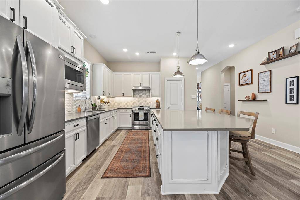 This modern kitchen features stainless steel appliances, upgraded cabinetry and a large central island with seating. The space is well-lit with pendant lights and under cabinet lighting.