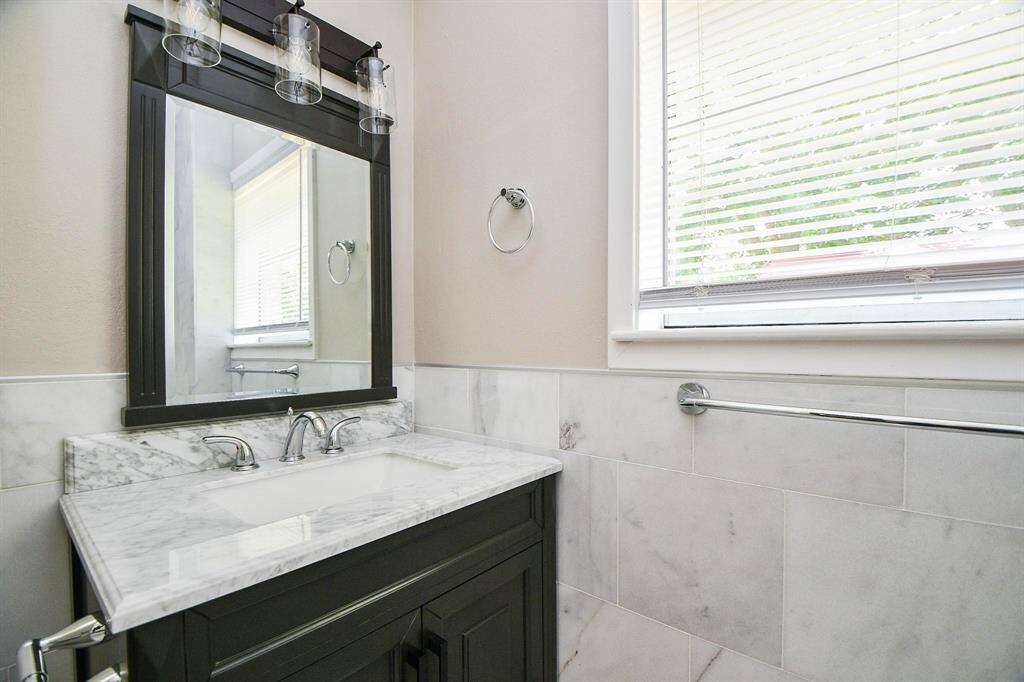 2nd full bath decorated tile, vanity are and sunlight.