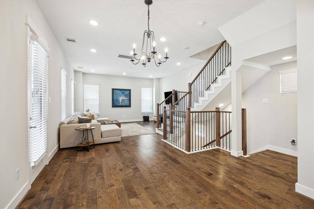 Spacious and bright living area and dining area with hardwood floors, updated lighting, and an elegant staircase with metal railings, ample natural light from multiple windows, and a neutral color palette.