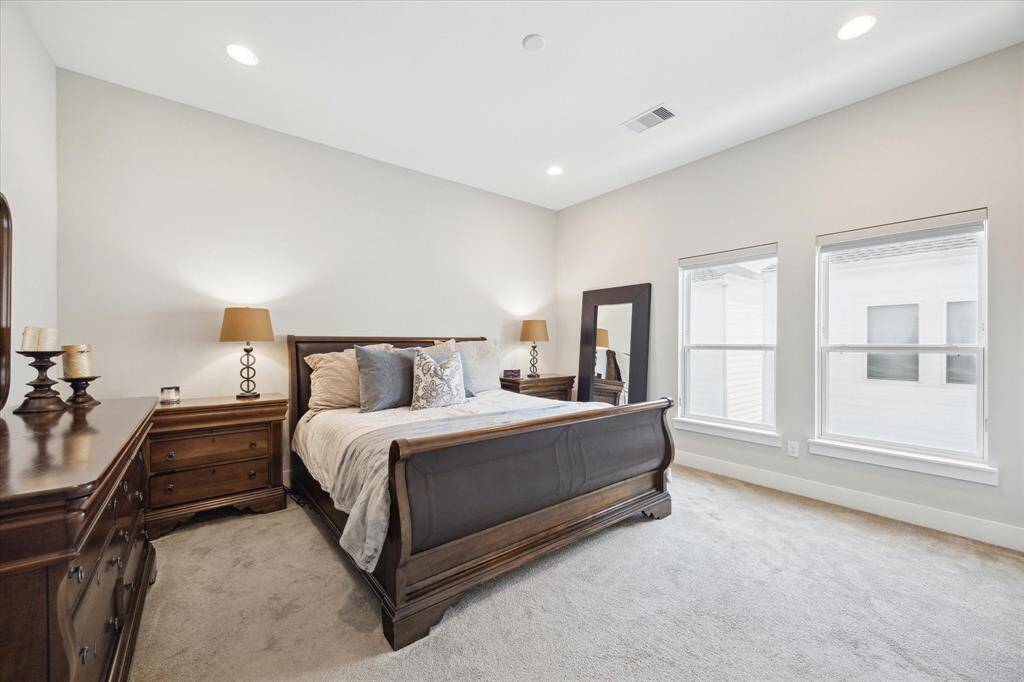 A spacious, bright bedroom with neutral tones gets ample natural light from the two windows. Cozy and inviting atmosphere.