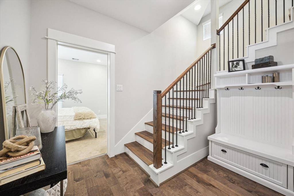 The inviting entry features a wooden staircase with upgraded black iron railings, and leads into the downstairs primary bedroom.